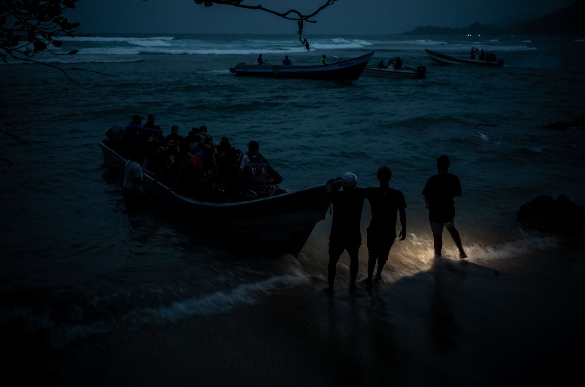 A group of Afghan, Chinese, Venezuelan, and Ecuadorian migrants wade toward a boat headed for the Darién Gap, in Capurganá, Colombia. Many of the Afghans had never seen the ocean before.&nbsp;